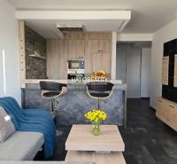 Nappali kétszobás lakásban nyitott konyhával és fa dekoros padlóval.