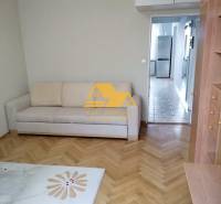 Nappali egy háromszobás lakásban fa dekor padlóval és világos kanapéval.