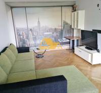 Nappali babapiskóta színű kanapéval, New York tapétával és fa dekor padlóval egy háromszobás lakásban.