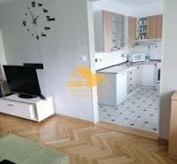 Nappali egy háromszobás lakásban, fa mintázatú padlóval és háttérben konyhával.