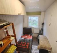 Kis szoba egy faházban ággyal, polccal és ablakkal, fa szekrényekkel és falakkal.