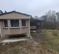 A Fő utcán található ház Újkelcsén, fákkal körülvéve és enyhén lejtős terepen.