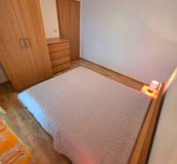 Hálószoba egy üdülőapartmanban, ággyal és bútorokkal fa dekor padlón.