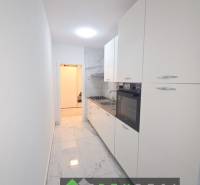 Keskeny fehér konyha főzőlappal és sütővel, márvány mintás padlóval egy háromszobás lakásban.