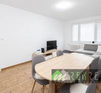 Nappali egy háromszobás lakásban, fa mintázatú padlóval és szürke kanapéval.