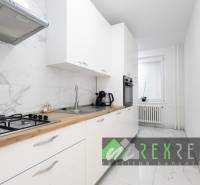 Konyha fehér szekrényekkel, márvány padlóval és beépített készülékekkel egy háromszobás lakásban.