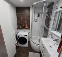 Fürdőszoba mosógéppel, zuhanyzóval és modern burkolattal egy háromszobás lakásban.