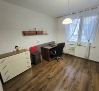 Dolgozószoba egy háromszobás lakásban fa hatású padlóval, asztallal és székkel.