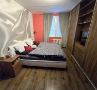 Hálószoba ággyal, beépített szekrényekkel és fa dekoros padlóval egy háromszobás lakásban.