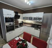 Konyha egy háromszobás lakásban fehér szekrényekkel, rozsdamentes acél készülékekkel és dekorációval az asztalon.