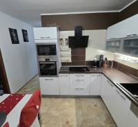 Konyha egy háromszobás lakásban lámpákkal, fehér szekrényekkel és csempével.