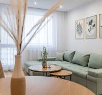 Világos nappali egy kétszobás lakásban zöld kanapéval és dekorációkkal a falon.