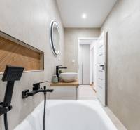 Fürdőszoba egy kétszobás lakásban káddal, mosdóval és kerek tükörrel.