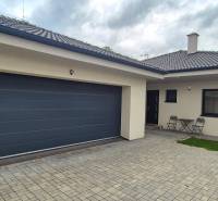 Családi ház Studienkában két székkel és egy asztallal a kövezett udvaron.