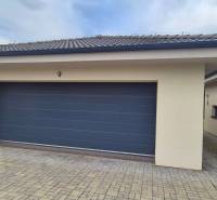 Garázs térkővel a családi ház mellett Studienkában, kőburkolattal és szürke kapuval.