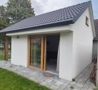 Családi ház Studienkában fehér homlokzattal és ferde tetővel, zöld fákkal körülvéve.