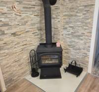 Kandalló a szoba sarkában kőburkolattal és fa dekorációjú padlóval.