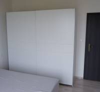 Egy családi ház szobája ággyal, fehér szekrénnyel és sötét ajtókkal.