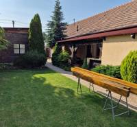 Családi ház Vámosladányban, gyep, bokrok és egy fa pad a kertben.