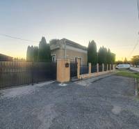 Családi ház Gútán magas tujafákkal és fém kerítéssel az út mellett.