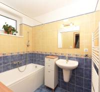 Fürdőszoba családi házban káddal, mosdóval, csempével és virágos ablakkal.