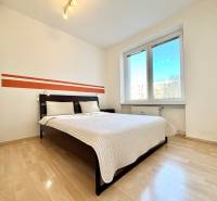 Hálószoba nagy ággyal, fehér falakkal és fa mintázatú padlóval.