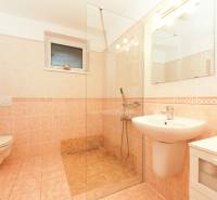 Fürdőszoba családi házban WC-vel, zuhanyzóval és mosdóval világos csempén.