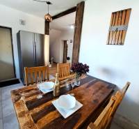 Családi ház konyhájában étkezőasztal kiegészítőkkel és hűtőszekrény.