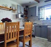 Konyha egy családi házban, faasztallal, székekkel és szürke szekrényekkel.