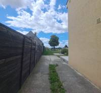 Családi ház Nagycsaládon a fakerítés mellett, betonút, felhők és fa.