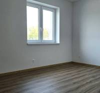 Szoba egy családi házban, fa mintázatú padlóval és fehér falakkal.