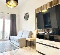 Nappali kanapéval és televízióval egy üdülő apartmanban, világos csempe, erkélyajtók.