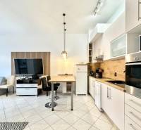 Rekreációs apartman belső tere konyhasarokkal, étkezőasztallal és falra szerelt televízióval.