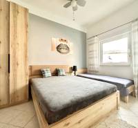 Világos hálószoba fa bútorokkal, franciaággyal és festménnyel egy üdülő apartmanban.