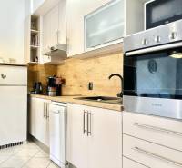 Konyha a nyaraló apartmanban fehér bútorokkal és fa dekorációval a falon.