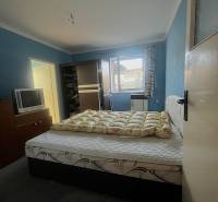 Hálószoba ággyal, sötét ruhásszekrénnyel, televízióval és kék falakkal egy családi házban.