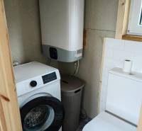 Fürdőszoba családi házban mosógéppel, bojlerrel és WC-vel. A padló dekoratív csempével van burkolva.