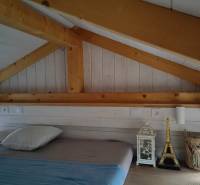 Tetőtéri hálószoba családi házban, fa mennyezettel és dekorációkkal az ágy mellett.