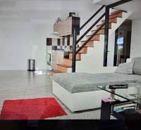 Nappali konyhasarokkal, lépcsővel, kanapéval, üvegasztallal és fa dekorú padlóval.