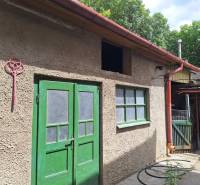 Családi ház Tachtán, két zöld ajtóval és világos árnyalatú homlokzattal.