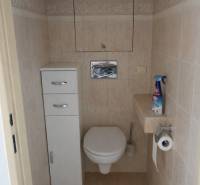 Világos csempékkel burkolt WC háromszobás lakásban tárolóhellyel.