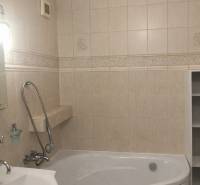 A háromszobás lakás fürdőszobája káddal és bézs falburkolattal.