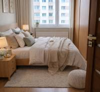 Hálószoba ággyal, szőnyeggel és fa dekorációjú padlóval egy háromszobás lakásban.