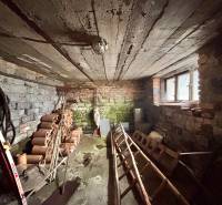 Családi ház alagsora téglafalakkal és mennyezettel, tárolt csövek és szerszámok.