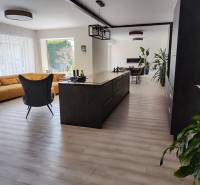 Konyha és nappali családi házban szigettel, sárga kanapéval és fa mintás padlóval.