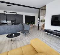 Nappali konyhával egy családi házban, fa dekoros padlóval és sárga kanapéval.