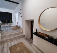 Családi ház belső tere fa dekorációjú padlóval, kerek tükörrel és szobanövényekkel.