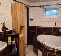 Fürdőszoba sarokkáddal, fehér mosdóval és fa bútorokkal egy családi házban.