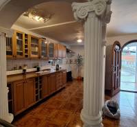 Családi ház belső tere fa konyhabútorral, oszlopokkal és fa dekorációjú padlóval.