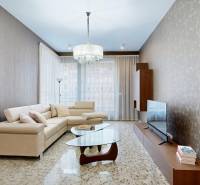 Nappali egy háromszobás lakásban bézs kanapéval, üveg asztallal és televízióval.